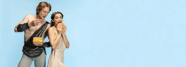 Burger and fast food. Young couple of ballet dancers in ancient Rome costums at blue studio. — Stock Photo, Image