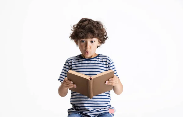 Un niño preescolar caucásico sentado y leyendo un libro aislado sobre fondo blanco del estudio. Copyspace. Infancia, educación, concepto de emociones —  Fotos de Stock