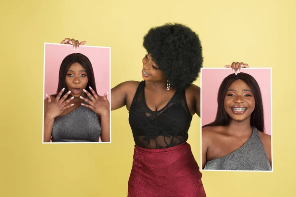 Joven chica africana sosteniendo sus retratos aislados sobre fondo de estudio amarillo con copyspace para el anuncio. Concepto de belleza, moda. —  Fotos de Stock