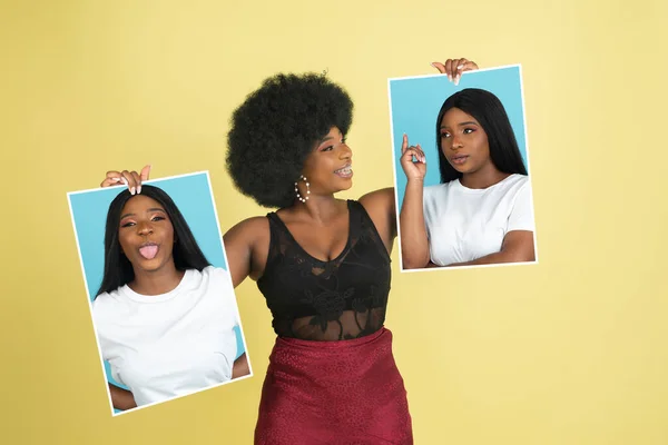 Joven chica africana sosteniendo sus retratos aislados sobre fondo de estudio amarillo con copyspace para el anuncio. Concepto de belleza, moda. —  Fotos de Stock