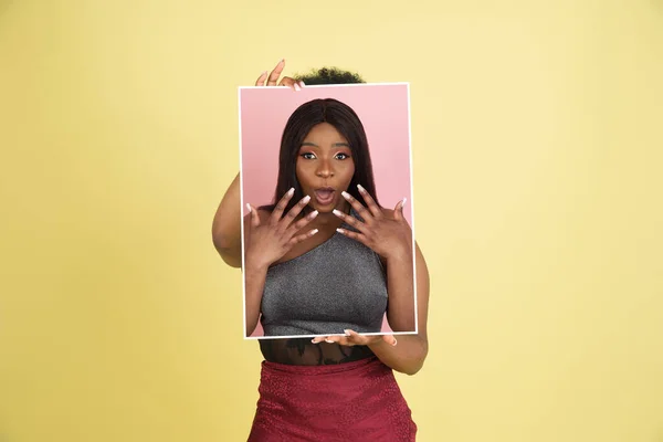 Chica africana joven sosteniendo su retrato aislado sobre fondo de estudio amarillo con copyspace para el anuncio. Concepto de belleza, moda. —  Fotos de Stock