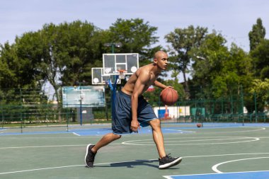 Strong muscular african-american male basketball player training at street public stadium, sport court or palyground outdoors. Summer sport games. clipart