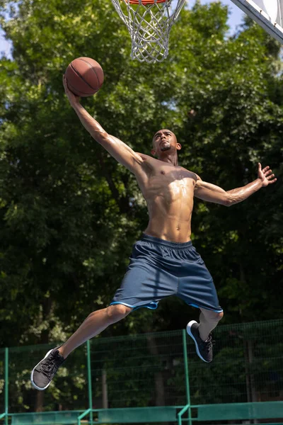 Fuerte musculoso afroamericano jugador de baloncesto masculino de entrenamiento en el estadio público de la calle, cancha deportiva o palyground al aire libre. Juegos de verano deporte. — Foto de Stock