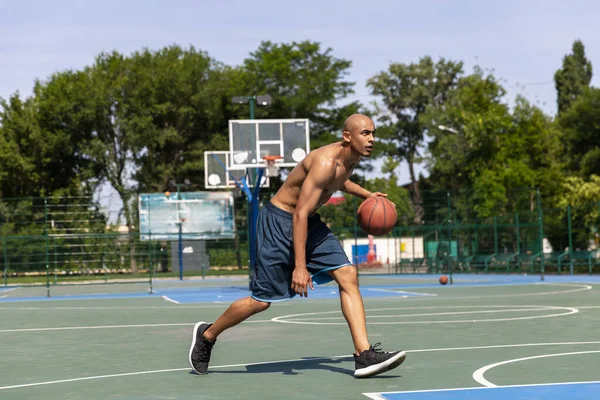 Fuerte musculoso afroamericano jugador de baloncesto masculino de entrenamiento en el estadio público de la calle, cancha deportiva o palyground al aire libre. Juegos de verano deporte. —  Fotos de Stock