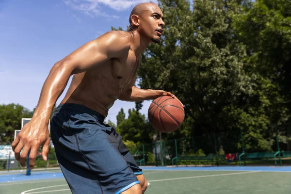 Primer plano joven, jugador de baloncesto africano masculino jugando baloncesto en el estadio público de la calle, pista de deporte o palyground al aire libre. Juegos de verano deporte. —  Fotos de Stock