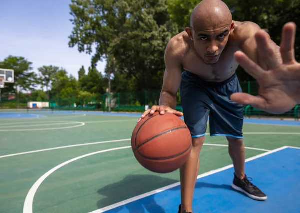 Alto, defensa. Hombre joven, jugador de baloncesto masculino africano musculoso que juega baloncesto en el estadio público de la calle, cancha deportiva o palyground al aire libre. Juegos de verano deporte. —  Fotos de Stock