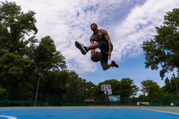 Junger Mann, muskulöser afrikanischer Basketballspieler, der im öffentlichen Straßenstadion, auf dem Sportplatz oder im Freien Basketball spielt. Sommersportspiele. — Stockfoto