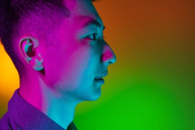 Asyalı genç adamın yakın çekimi stüdyo arka planında izole edilmiş yeşil ışık, renk filtresi. İnsan duyguları kavramı, yüz ifadesi.