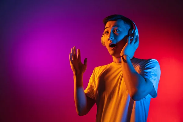Bir Asyalı genç adam stüdyo arka planında izole edilmiş. Gradyan pembe neon ışığı, renk filtresi. İnsan duyguları kavramı, yüz ifadesi. — Stok fotoğraf