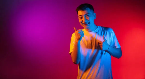 Un jeune homme asiatique isolé sur fond studio dans un dégradé de lumière rose-violet néon, filtre de couleur. Concept d'émotions humaines, expression faciale. — Photo