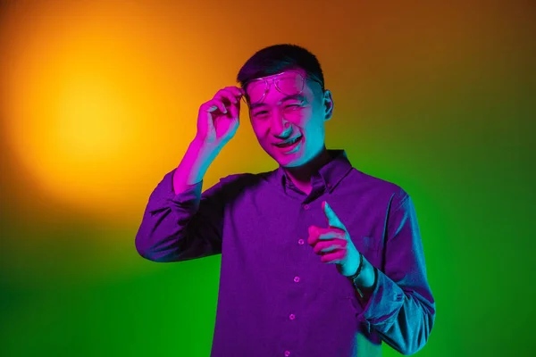 Portret młodego Azjaty odizolowanego na tle studia w gradientowym, zielonym, żółtym neonie, kolorowym filtrze. Pojęcie ludzkich emocji, wyraz twarzy. — Zdjęcie stockowe