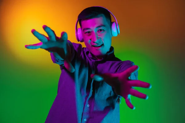 Portret młodego Azjaty odizolowanego na tle studia w gradientowym, zielonym, żółtym neonie, kolorowym filtrze. Pojęcie ludzkich emocji, wyraz twarzy. — Zdjęcie stockowe