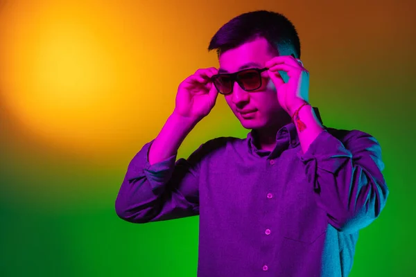 Hübscher junger Mann in Sonnenbrille, isoliert auf Studiohintergrund im Farbverlauf grün-gelb Neonlicht, Farbfilter. Konzept menschlicher Emotionen, Mimik. — Stockfoto
