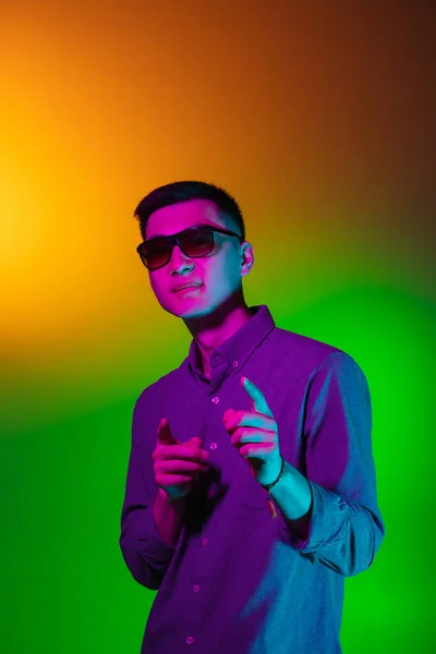 Przystojny młody człowiek w okularach przeciwsłonecznych odizolowany na tle studia w gradientowym zielonym żółtym świetle neonowym, kolorowy filtr. Pojęcie ludzkich emocji, wyraz twarzy. — Zdjęcie stockowe