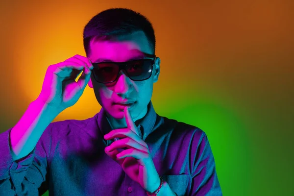 Portrait de jeune homme asiatique isolé en studio dans un dégradé de lumière jaune néon vert, filtre de couleur. Concept d'émotions humaines, expression faciale. — Photo