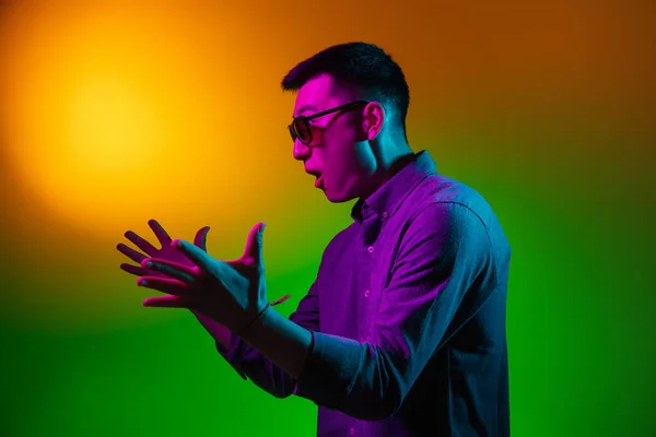 Porträtt av asiatisk ung man isolerad på studio bakgrund i gradient grön neon ljus, färgfilter. Begreppet mänskliga känslor, ansiktsuttryck. — Stockfoto