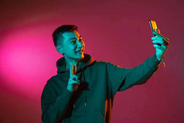 Portrait mi-long d'un jeune homme asiatique isolé en studio dans une lumière rouge fluo dégradée, filtre couleur. Concept d'émotions humaines, expression faciale. — Photo