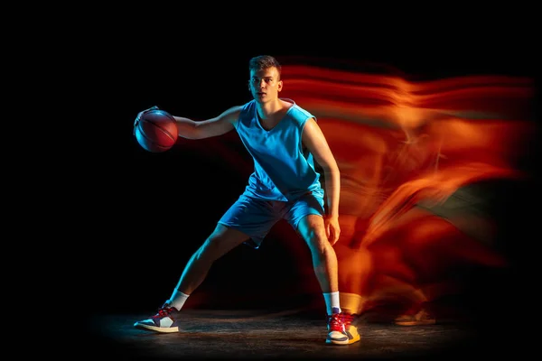 年轻的高加索男性篮球运动员在昏暗的工作室背景下在混光中打篮球。健康生活方式、职业运动、业余爱好的概念. — 图库照片