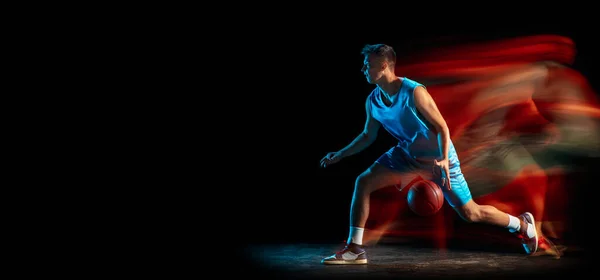 플라이어. 젊은 코카 시안 남자 농구 선수가 어두운 스튜디오 배경에서 혼합 된 빛으로 격리되어 농구를 하고 있습니다. 건강 한 생활 방식, 직업적 인 스포츠, 취미의 개념. — 스톡 사진