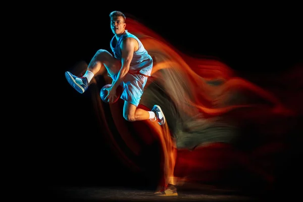 Ung kaukasisk manliga basketspelare spelar basket isolerad över mörk studio bakgrund i blandat ljus. Begreppet hälsosam livsstil, professionell idrott, hobby. — Stockfoto