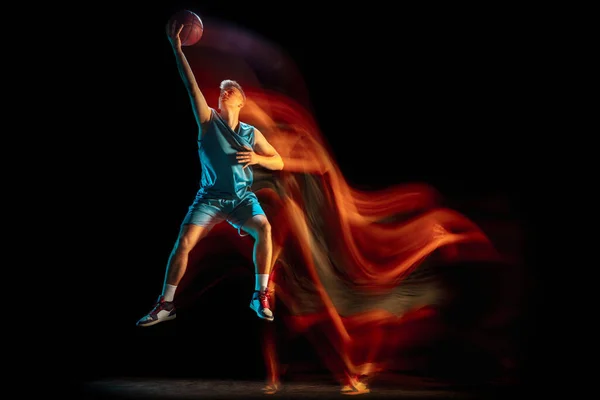 Jonge blanke man basketbalspeler die basketbal speelt geïsoleerd over donkere studio achtergrond in gemengd licht. Concept van gezonde levensstijl, professionele sport, hobby. — Stockfoto