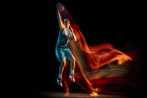 Młody biały mężczyzna, koszykarz grający w koszykówkę w ciemnym studio w mieszanym świetle. Pojęcie zdrowego stylu życia, sportu zawodowego, hobby. — Zdjęcie stockowe