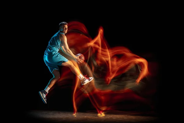 Jovem jogador de basquete masculino caucasiano jogando basquete isolado sobre fundo escuro estúdio em luz mista. Conceito de estilo de vida saudável, esporte profissional, hobby. — Fotografia de Stock