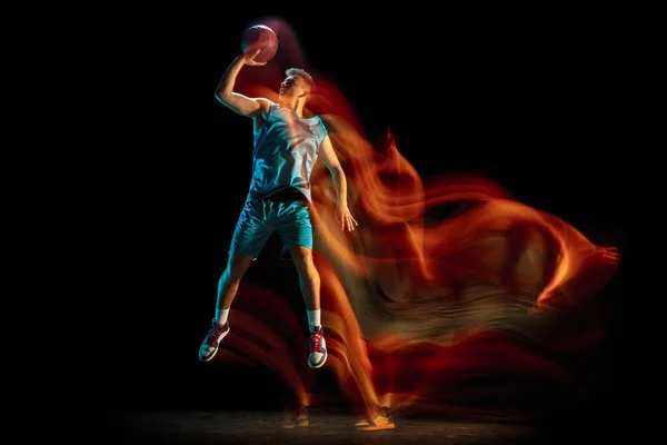 Молодой кавказский мужчина, баскетболист, играющий в баскетбол, изолирован на тёмном фоне студии в смешанном свете. Концепция здорового образа жизни, профессионального спорта, хобби. — стоковое фото