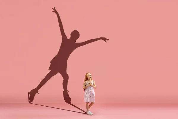 Childhood and dream about big and famous future. Conceptual image with girl and shadow of female figure skater on coral pink wall, background. — Stock Fotó