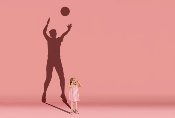 Childhood and dream about big and famous future. Conceptual image with little girl and shadow of female volleyball player on coral pink wall, background. — Stock Photo, Image