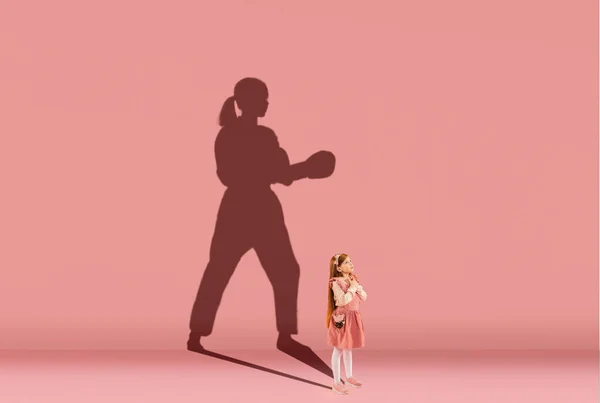 Παιδική ηλικία και όνειρο για μεγάλο και διάσημο μέλλον. Εννοιολογική εικόνα με το κορίτσι και τη σκιά του ισχυρού θηλυκό taekwondo ασκούμενος σε κοραλλιογενή ροζ φόντο — Φωτογραφία Αρχείου