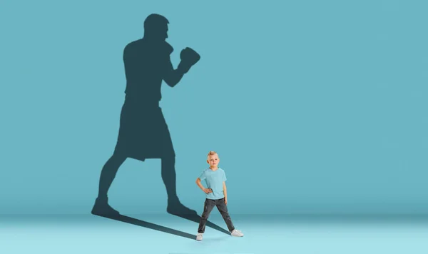 Childhood and dream about big and famous future. Conceptual image with boy and shadow of strong male boxer on blue background. Dreams, imagination, education concept. — Stock Photo, Image