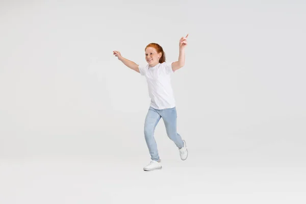 漂亮可爱的小红头发女孩穿着休闲装跑步。在白色工作室背景上独立播放。快乐童年的概念。阳光般的孩子 — 图库照片