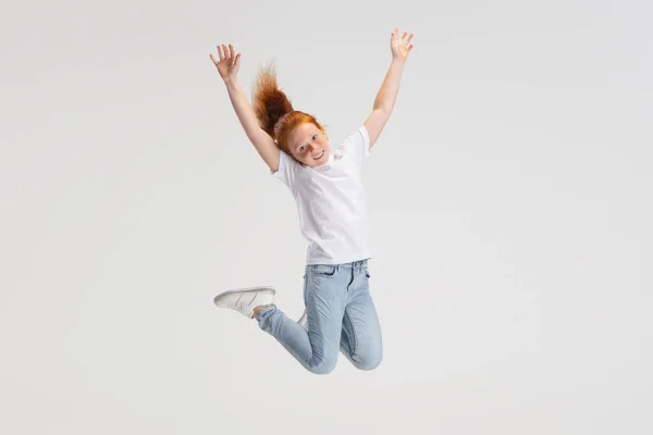 Beautiful cute little red-headed girl in casual outfit jumping isolated on white studio background. Happy childhood concept. Sunny child — стоковое фото