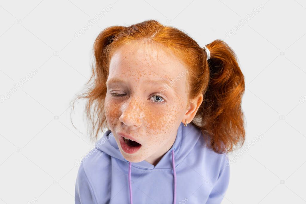 Close-up funny girl with freckled face and red hair looking at camera isolated on white studio background. Happy childhood concept. Sunny child