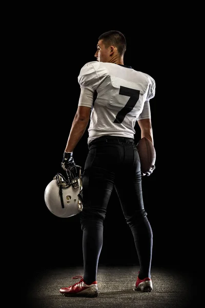 Portret jonge Amerikaanse voetballer, atleet in zwart wit sportuniform poseren geïsoleerd op donkere studio achtergrond. Begrip professionele sport, kampioenschap, competitie. — Stockfoto