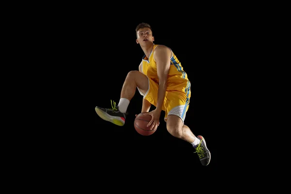 Vysoký skok. Basketbalista s míčem v akci a pohybu izolované na tmavě černém pozadí studia. Koncept reklamy. Silný bělošský atlet trénující s basketbalem. — Stock fotografie