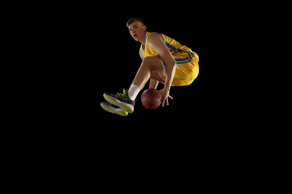 Jump shot. Basketball player with a ball in action and motion isolated on dark black studio background. Advertising concept. Strong Caucasian athlete practicing with basketball ball.