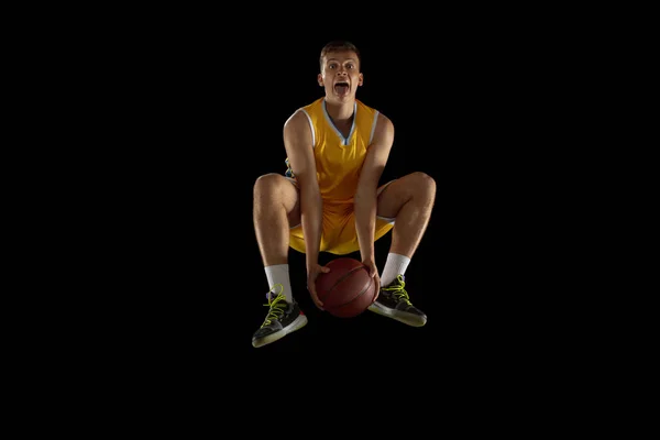 Sprong schot. Basketbalspeler met een bal in actie en beweging geïsoleerd op donker zwarte studio achtergrond. Reclame concept. Sterke Kaukasische atleet oefenen met basketbal. — Stockfoto