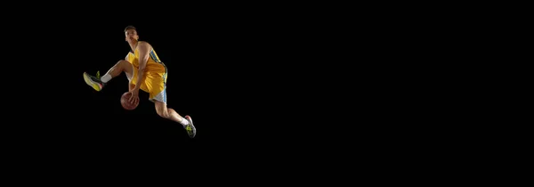 Skacz. Koszykarz z piłką w akcji i ruch izolowany na ciemnym czarnym tle studio. Koncepcja reklamy. Silny biały sportowiec ćwiczący z piłką do koszykówki. — Zdjęcie stockowe