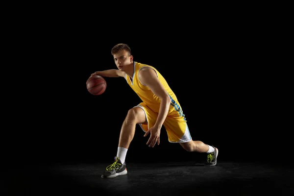 Jugador de baloncesto con un entrenamiento de pelota aislado sobre fondo de estudio negro oscuro. Concepto publicitario. Ajuste atleta caucásico practicando con pelota. — Foto de Stock