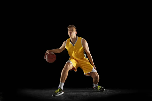 Basket spelare med en boll i aktion och rörelse isolerad på mörk svart studio bakgrund. Reklamkoncept. Stark kaukasisk idrottare tränar med basket. — Stockfoto