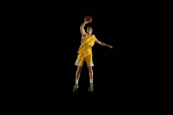 Hombre joven, jugador de baloncesto con un entrenamiento de pelota aislado sobre fondo negro oscuro estudio. Concepto publicitario. Ajuste atleta caucásico practicando con pelota. —  Fotos de Stock