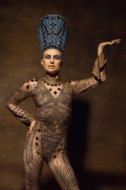 Nefertiti 'nin sanat performansındaki görüntüsü gibi güzel genç bir kadın. Kahverengi renkli arka planda izole edilmiş. Retro biçimi, dönemin karşılaştırması.