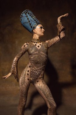 Nefertiti 'nin sanat performansındaki görüntüsü gibi güzel genç bir kadın. Kahverengi renkli arka planda izole edilmiş. Retro biçimi, dönemin karşılaştırması.