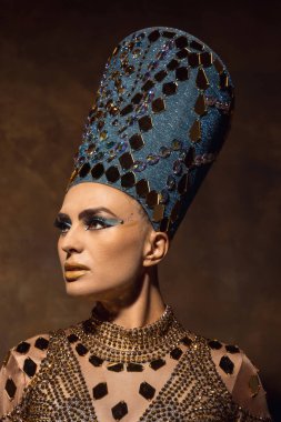 Nefertiti 'nin sanat performansını gösteren yakın plan güzel bir genç kadın. Kahverengi renkli arka planda izole edilmiş. Retro biçimi, dönemin karşılaştırması.