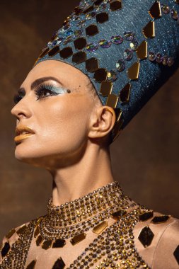Nefertiti 'nin sanat performansını gösteren yakın plan güzel bir genç kadın. Kahverengi renkli arka planda izole edilmiş. Retro biçimi, dönemin karşılaştırması.