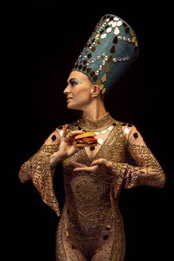 Nefertiti 'nin sanat performansını yansıtan genç ve güzel bir kadın karanlık arka planda modern fast food tadıyor. Retro tarzı, çağların karşılaştırılması, mizah anlayışı.