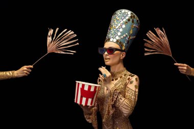 Sanat performansında Nefertiti 'nin görüntüsü olan genç bir kadın karanlık arka planda izole edilmiş bir film izliyor. Retro tarzı, çağların karşılaştırılması, mizah anlayışı.