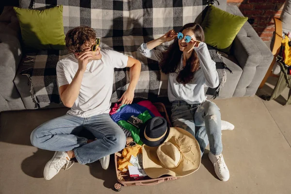 Jovem e menina feliz, casal experimentando trajes, roupas para férias de verão sentado em casa, dentro de casa. Tomar a decisão certa. Olha animado, encantado. — Fotografia de Stock